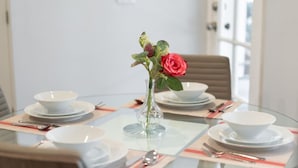 A round glass table with white plates, bowls, and cutlery. A clear vase with a red rose and green leaves is centered on the table. - 1BR House in Glendale With Private Fenced Yard p55 (Glendale)