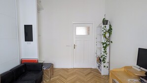 Ein Zimmer mit einer weißen Tür, einem schwarzen Sofa, einem roten Sessel, einem Holztisch und einer Pflanze auf einem Regal.