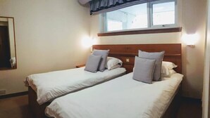 Een hotelkamer met twee enkele bedden, een houten hoofdeinde, een raam met gordijn en een spiegel aan de muur.
