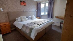 A bedroom with a bed, nightstand, dresser, and a window with curtains. - Highland Lodge 04 Loch Rannoch Highland Club (Pitlochry)