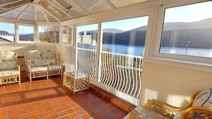 A sunroom with a view of a lake and mountains, furnished with wicker chairs and a small table. - Highland Lodge 04 Loch Rannoch Highland Club (Pitlochry)