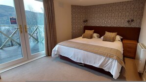 A bedroom with a bed, a nightstand, a radiator, a window with curtains, and a view of a deck.