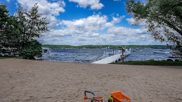 A sandy beach with a dock extending into a lake, surrounded by trees. - Windmill Cottage at Abbey Springs Near Lake & Shops! (Fontana)