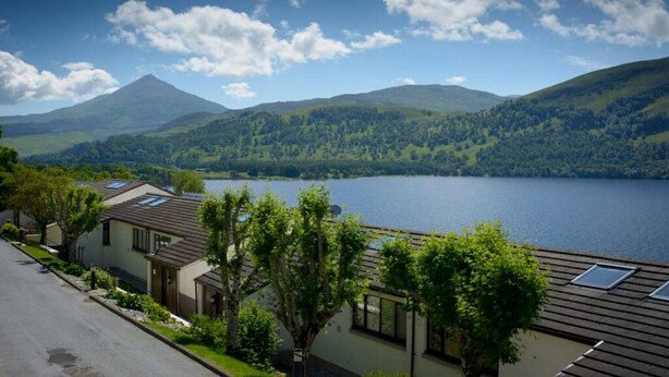 Vista sobre un lago con una montaña al fondo, una hilera de casas con techos inclinados y un cielo despejado.