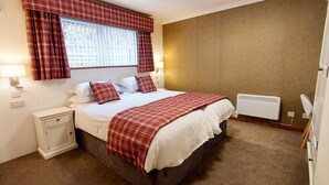A bedroom with a bed, nightstand, lamp, window with curtains, and a radiator. - Otter Lodge 07 Loch Rannoch Highland Club (Pitlochry)