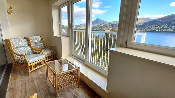 A balcony with wicker furniture and a glass table, overlooking a lake and mountains. - Otter Lodge 07 Loch Rannoch Highland Club (Pitlochry)