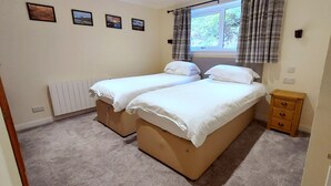 Ein Schlafzimmer mit zwei Einzelbetten, einem Fenster mit Vorhängen, einem Heizkörper und einem kleinen Nachttisch.