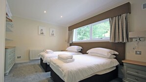 A bedroom with two beds, a window with curtains, a radiator, and a dresser. - Pine Marten Lodge 02 Loch Rannoch Highland Club (Pitlochry)