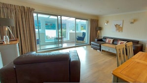 A modern living room with a sofa, a dining table, and a kitchen area with appliances. - Pine Marten Lodge 02 Loch Rannoch Highland Club (Pitlochry)