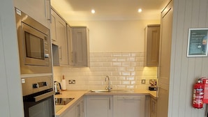 A modern kitchen with stainless steel appliances, white cabinetry, and a wooden floor. - Pine Marten Lodge 02 Loch Rannoch Highland Club (Pitlochry)