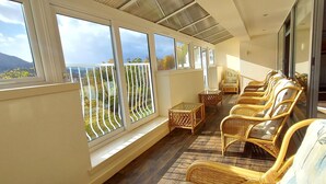 Ein sonnendurchflutetes Zimmer mit großen Fenstern, Korbmöbeln und Blick ins Freie.