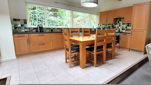 Una cocina con armarios de madera, una mesa de comedor con sillas y una ventana con vistas a la vegetación.