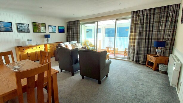 A spacious living room with a wooden dining table, two armchairs, a sofa, and a balcony with a view. - Red Deer Lodge 04 Loch Rannoch Highland Club (Pitlochry)