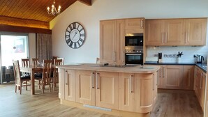 A modern kitchen with wooden cabinets, a central island, and a built-in oven. - Highland Lodge 06 Loch Rannoch Highland Club (Pitlochry)