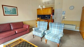 Ein Wohnzimmer mit einem roten Ledersofa, zwei karierten Sessel, einem Holztisch und einem Gemälde an der Wand.
