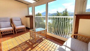 Ein Balkon mit Korbmöbeln, einem Glastisch und Blick auf die Berge.