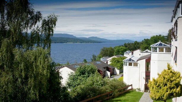 Eine Wohngegend am Seeufer mit weißen Häusern, einige davon mit Solaranlagen, und Blick auf den See und die entfernten Berge.