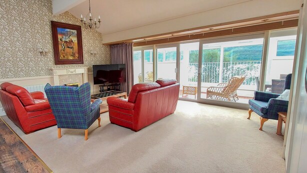 A living room with a fireplace, a television, and a balcony with outdoor furniture. - Highland Lodge 40 Loch Rannoch Highland Club (Pitlochry)
