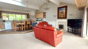 A spacious living area with a red leather sofa, a dining table with chairs, a kitchen with wooden cabinets, and a fireplace. - Highland Lodge 40 Loch Rannoch Highland Club (Pitlochry)