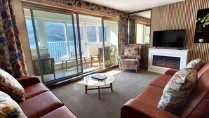 Un soggiorno con divano, camino, televisione e un balcone con vista sulle montagne.