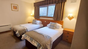 A twin bedroom with two beds, a window with curtains, bedside lamps, a framed picture on the wall, and a radiator. - Otter Lodge 06 Loch Rannoch Highland Club (Pitlochry)