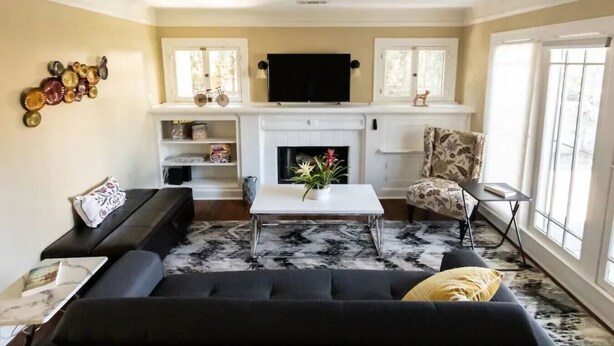 Ein Wohnzimmer mit schwarzem Sofa, weißem Couchtisch, Kamin und einem darüber montierten Fernseher.