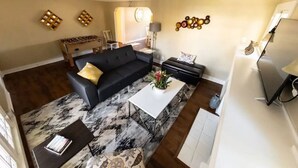 Ein Wohnzimmer mit einer schwarzen Couch, einem weißen Couchtisch und einem gemusterten Teppich.