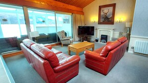 A living room with red leather sofas, a wooden coffee table, a fireplace, and a television. - Highland Lodge 07 Loch Rannoch Highland Club (Pitlochry)