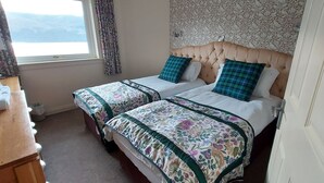 A hotel room with two beds, floral bedspreads, a wooden dresser, a window with a view, and patterned wallpaper. - Highland Lodge 07 Loch Rannoch Highland Club (Pitlochry)