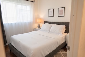 A neatly made bed with white linens, a bedside lamp, and two framed pictures on the wall. - Spacious 4-bedroom Home With Large Yard AND Garage Near Knott S Berry Farm p67 (Cypress)