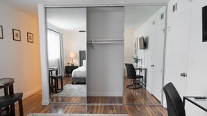 Una moderna camera d'albergo con un'ampia porta scorrevole che dà su una zona notte, una scrivania con sedia, una TV a parete e un comodino con lampada.