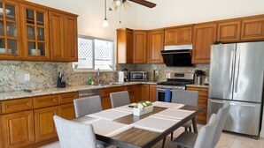 Una cucina moderna con mobili in legno, piani in granito, elettrodomestici in acciaio inossidabile e un'area pranzo con tavolo e sedie.