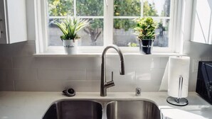 A kitchen with a double sink, a stainless steel faucet, and two potted plants on the windowsill. - Tranquil 2BR Home in Beautiful Neighborhood P24 (Burbank)