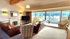 A living room with a fireplace, television, and a view of a snowy landscape through large windows.