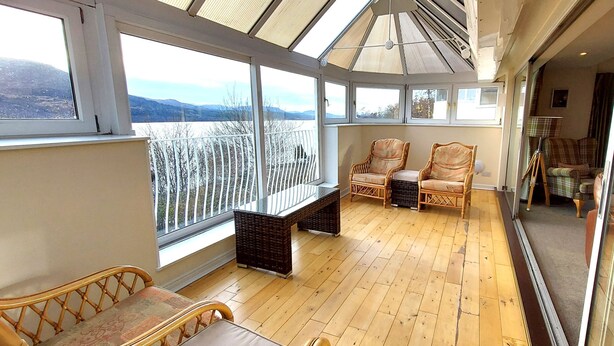 A sunroom with large windows, wicker furniture, and a view of a snowy landscape.