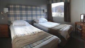 A hotel room with two beds, a wooden nightstand, a desk with a mirror, and a window with curtains.