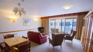 A cozy living room with a sofa, chairs, a TV, and a balcony with curtains. - Otter Lodge 04 Loch Rannoch Highland Club (Pitlochry)