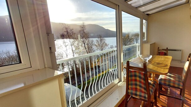 Ein Balkon mit Seeblick und Bergblick, ein Tisch mit Stühlen und eine kleine Tischlampe.