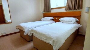 Et hotelværelse med to senge, en træsenggavl, et stort spejl og et vindue med gardiner.