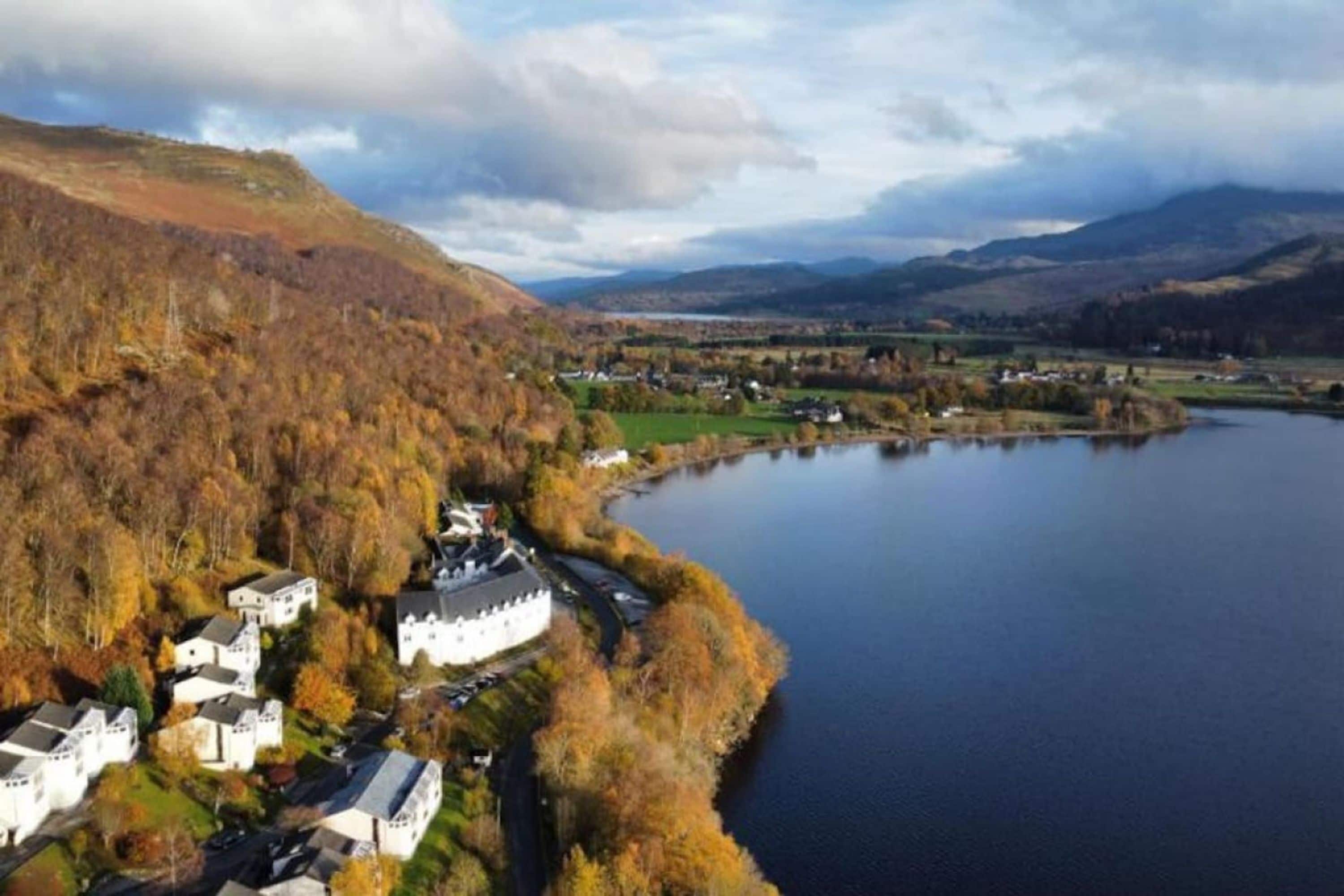 Une propriété au bord du lac, avec un grand bâtiment blanc, entourée d’un feuillage automnal et bordée d’un lac paisible.