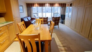 A dining area with a wooden table and chairs, a sofa, and a television. - Studio 03 Loch Rannoch Highland Club (Pitlochry)