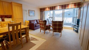 A cozy living room with a dining area, a sofa, plaid chairs, and a large window with a view. - Studio 03 Loch Rannoch Highland Club (Pitlochry)
