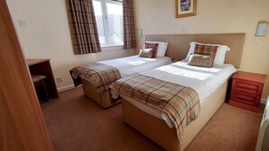 A double bed with a plaid blanket, a bedside table, and a small wooden cabinet. - Highland Lodge 43 Loch Rannoch Highland Club (Pitlochry)
