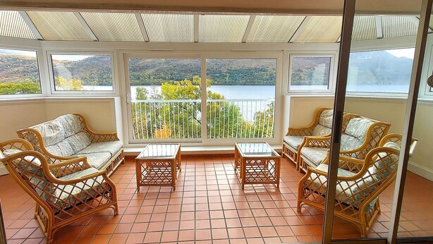 A balcony with wicker furniture and a view of a lake and hills. - Highland Lodge 43 Loch Rannoch Highland Club (Pitlochry)