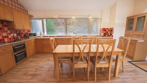 A modern kitchen with wooden cabinets, a dining table with chairs, and a large window with blinds. - Highland Lodge 43 Loch Rannoch Highland Club (Pitlochry)
