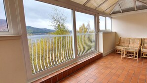Un balcon avec vue sur les arbres et les collines, un sol carrelé et des meubles en osier.