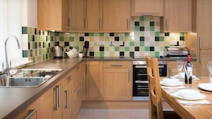 A modern kitchen with wooden cabinets, a tiled backsplash, stainless steel appliances, and a dining area set for a meal. - Osprey Lodge Loch Rannoch Highland Club (Pitlochry)