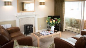 A living room with a fireplace, a television, and a coffee table with books and flowers. - Osprey Lodge Loch Rannoch Highland Club (Pitlochry)