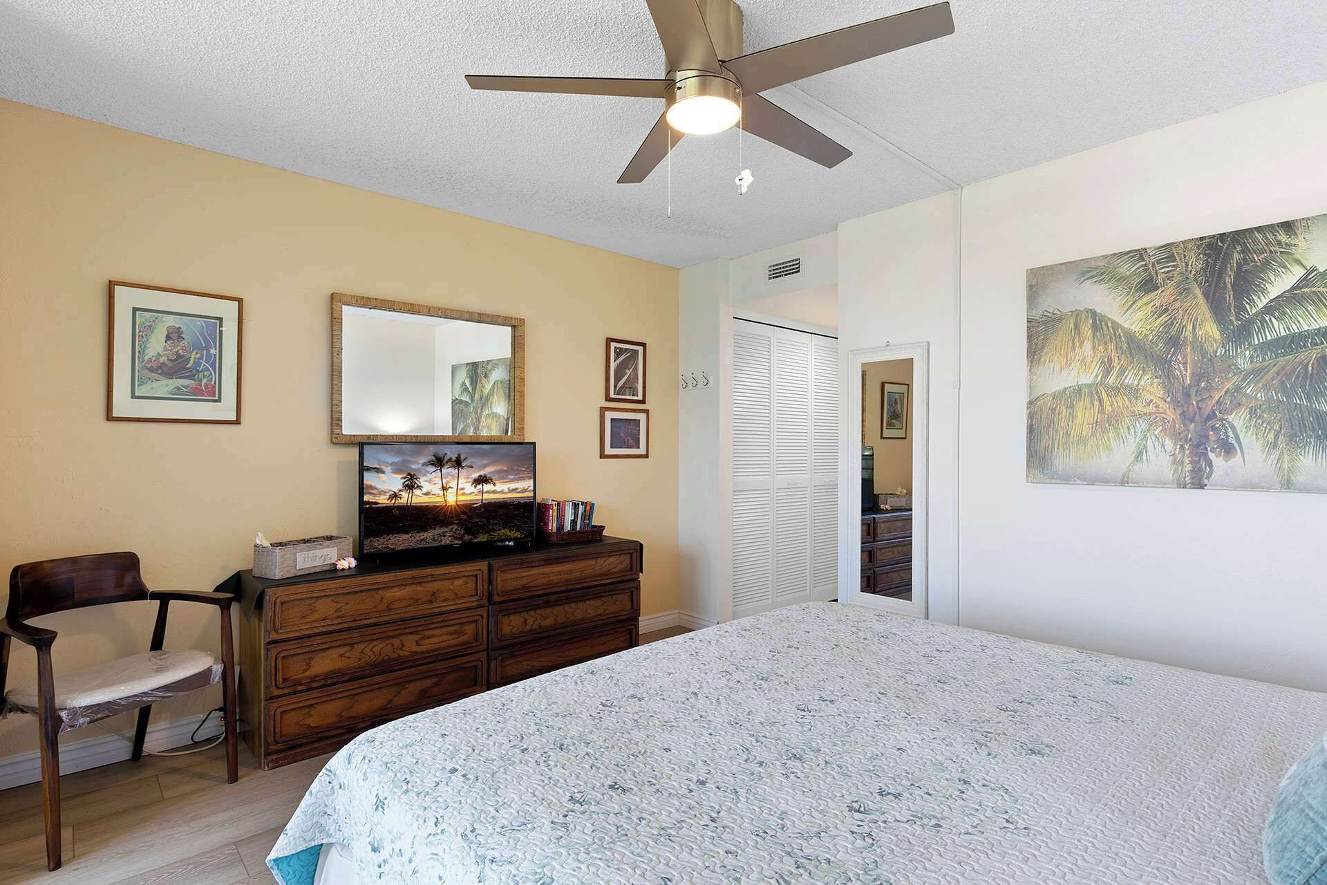 A bedroom with a bed, a dresser, a chair, a ceiling fan, and wall art.