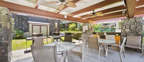 An outdoor patio with a round glass table and four chairs, a ceiling fan, and a stone wall.